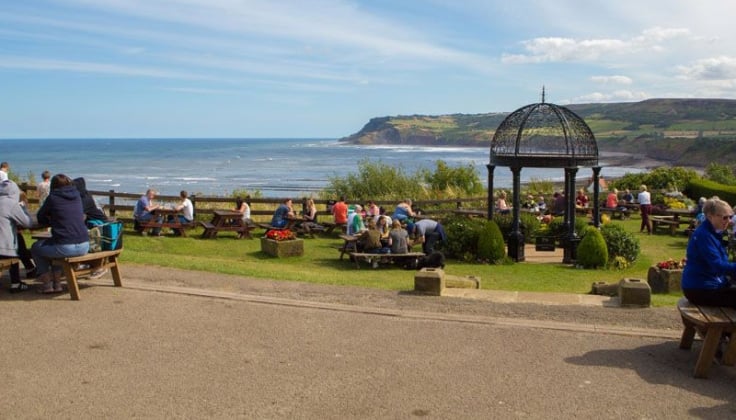 Picnic tables with people and gazebo set beside the seaside